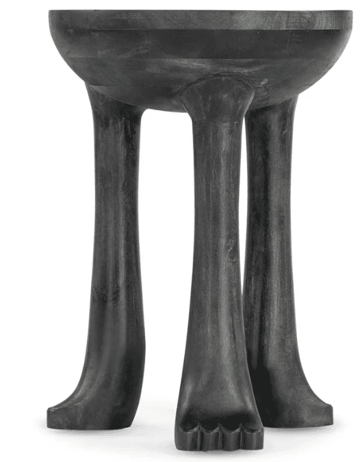 A dark, possibly ebonized, wooden pedestal table featuring a rounded, shallow bowl-like top. The table is supported by three robust, sculpted legs that splay outwards slightly and terminate in stylized foot-like carvings, complete with distinct toe details. The entire piece exhibits a hand-carved, organic aesthetic. — 3D model