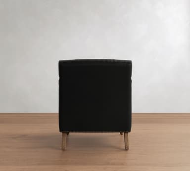 A traditional style armchair upholstered in black leather, featuring prominent brass nailhead trim along the armrests and base. The chair is supported by turned wooden legs and has exposed wooden arm supports, contributing to its classic aesthetic. — 3D model