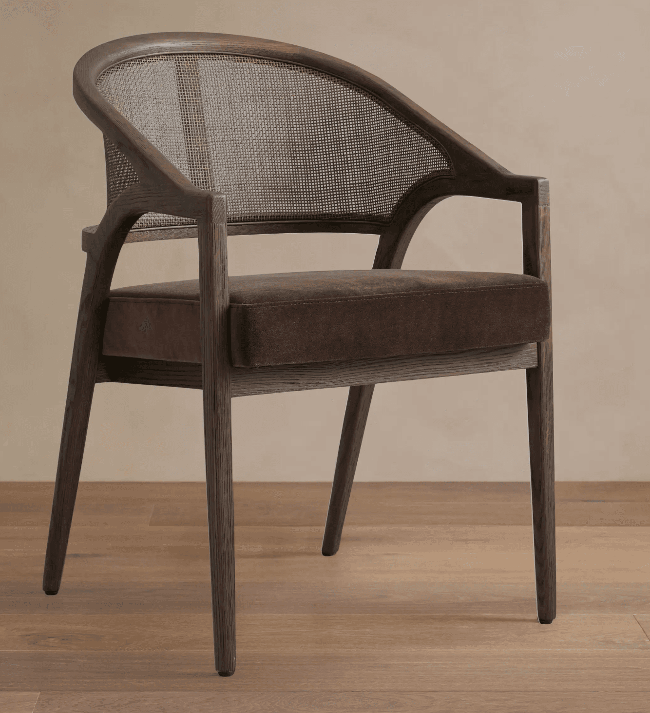 A wooden armchair with a cane back and upholstered seat. The chair features a curved backrest and armrests that flow into the legs. The frame appears to be made of dark stained wood, possibly oak, with a visible grain pattern. The seat is covered in a dark brown, plush fabric, possibly velvet or a similar material. The backrest is constructed from woven cane material, offering a textured contrast to the solid wood frame and upholstered seat. — 3D model