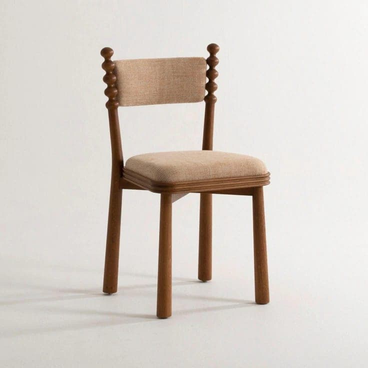 A contemporary dining chair featuring a solid wood frame with distinctive bobbin-turned back posts. The seat and backrest are upholstered in a light beige, textured fabric, providing comfort. The chair has straight, cylindrical legs and a minimalist, yet characterful design. — 3D model