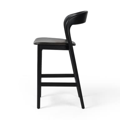 A contemporary bar stool with a black wooden frame and a dark upholstered seat. The stool features a gently curved backrest and a square footrest connecting the tapered legs. — 3D model