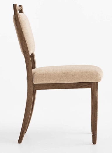 A traditional wooden dining chair featuring an upholstered seat and backrest, and a distinctive turned spindle top rail. The frame is made of dark brown wood, possibly oak, with visible grain. The seat and back are padded and covered in a light beige, textured fabric. The legs are tapered, with the back legs subtly splayed. — 3D model