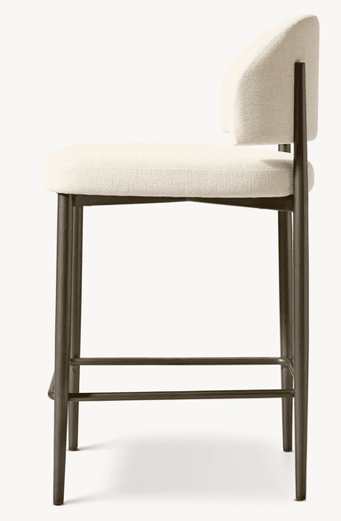 A contemporary bar stool featuring a light beige upholstered seat and a gently curved backrest, supported by a bronze-finished metal frame with an integrated square footrest. — 3D model