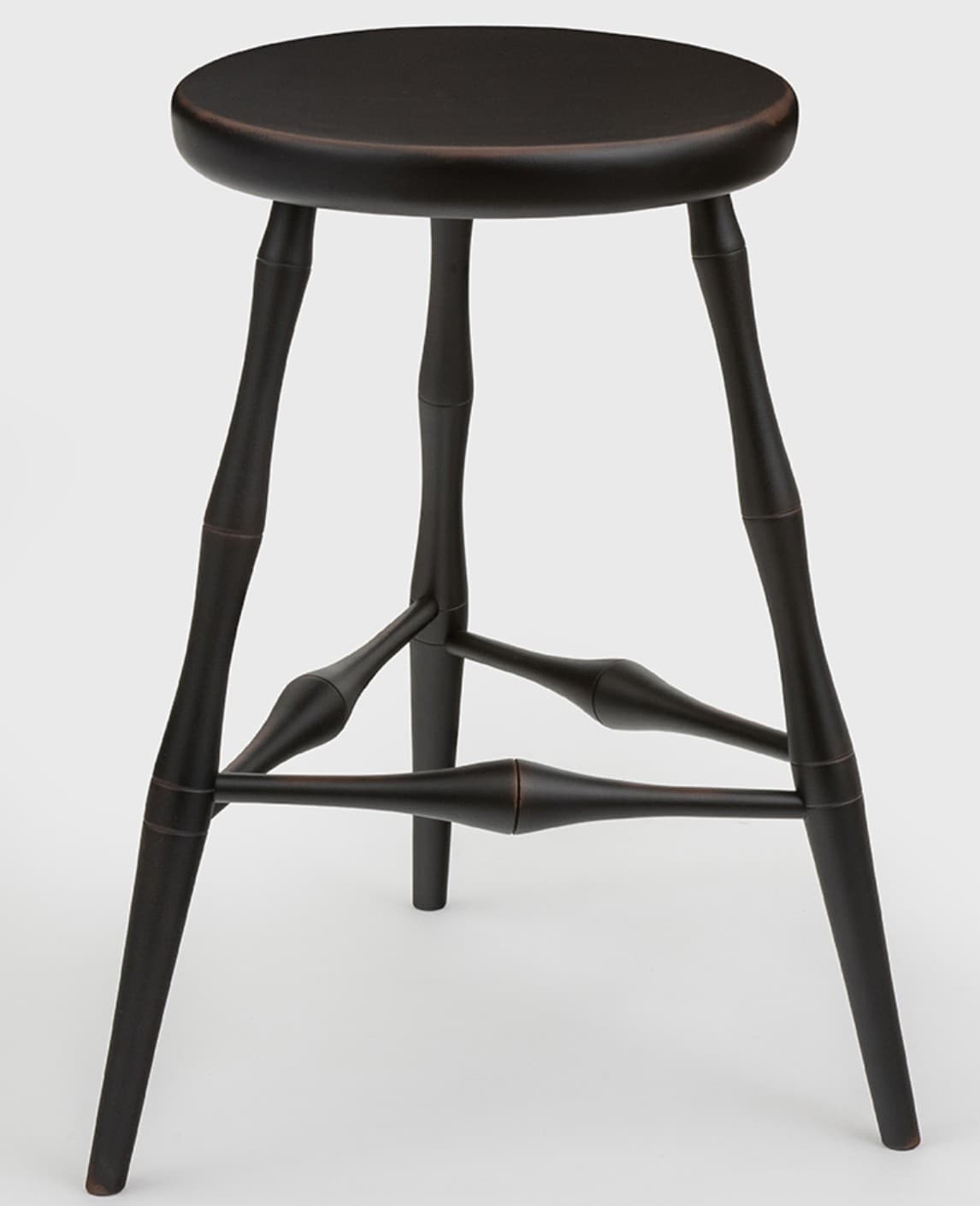 A dark, likely black-painted, wooden stool with a round seat and three splayed, turned legs. The legs are connected by three turned stretchers forming a triangular base. The finish appears matte or satin with subtle variations. — 3D model