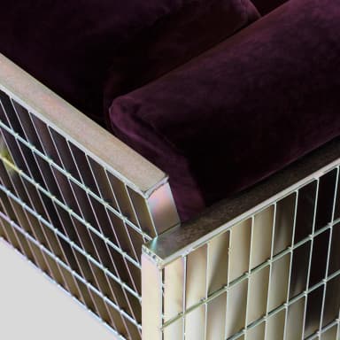 A modern sofa featuring a deep purple velvet upholstered seat and back, with rounded armrests. The frame and legs are constructed from polished metal, presenting a slatted design on the sides and base, giving it a distinct industrial or contemporary aesthetic. — 3D model
