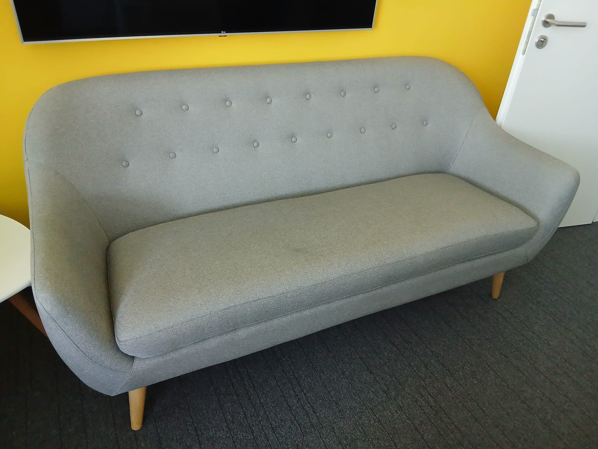 A contemporary loveseat upholstered in grey fabric, featuring a gracefully curved silhouette, button tufting on the backrest, and tapered wooden legs. It has a single, elongated seat cushion and fixed, rounded arms. — 3D model