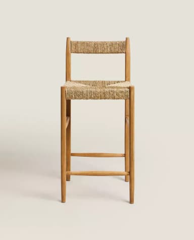 A tall bar stool constructed with a wooden frame and a woven natural fiber seat and backrest. The stool features a simple, minimalist design with straight legs connected by horizontal stretchers for stability. The seat and back are made of tightly woven rush or seagrass. — 3D model