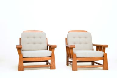 A pair of lounge chairs, each featuring a robust wooden frame with light-colored upholstered seat and back cushions. The back cushions are tufted with six buttons. The chairs display a sturdy, classic design with prominent wooden armrests and base structure. — 3D model