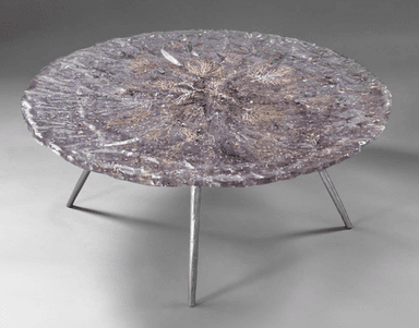 A circular coffee table with a dark, textured top featuring embedded organic or decorative elements. It is supported by three slender, metallic legs. — 3D model
