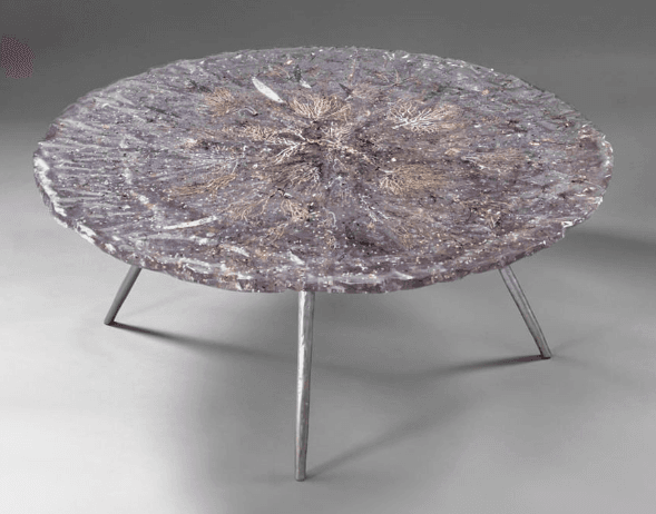 A circular coffee table with a dark, textured top featuring embedded organic or decorative elements. It is supported by three slender, metallic legs. — 3D model