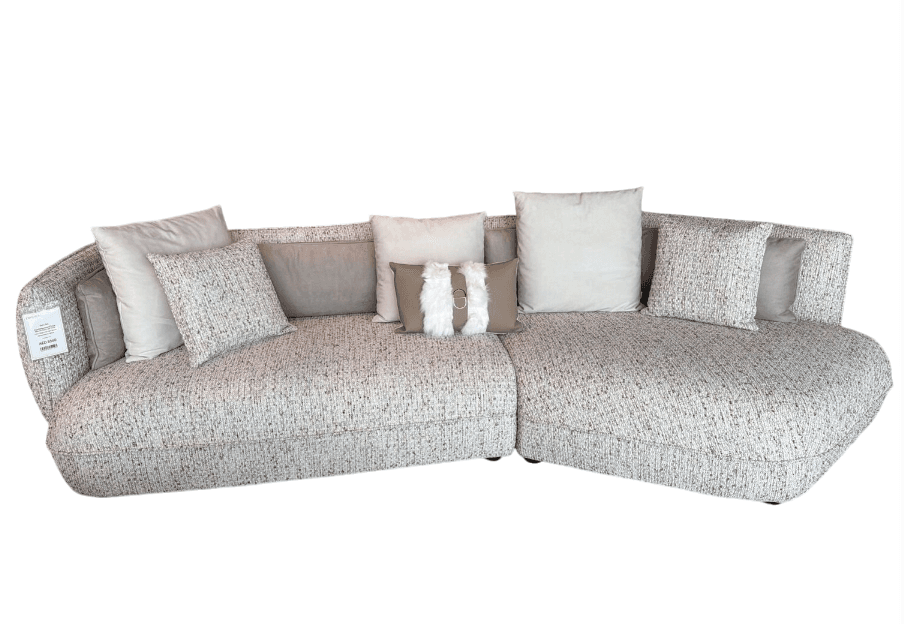 A large, modular sectional sofa with a curved silhouette. It features a speckled upholstery in a light neutral tone and includes several throw pillows of varying sizes and patterns, some with tasseled embellishments. The sofa appears to be designed for comfort and contemporary living spaces. — 3D model