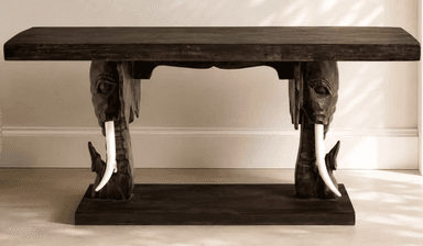 A dark wooden console table featuring intricately carved elephant heads as supports, complete with white tusks, connecting the tabletop to a lower base. — 3D model