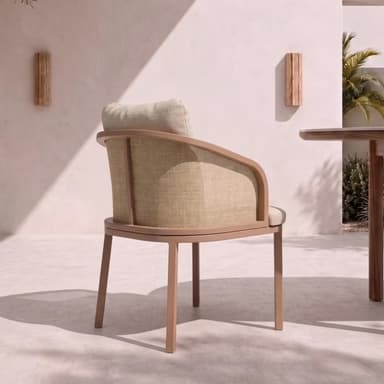A contemporary armchair featuring a metal frame with a light brown, wood-look finish. The backrest incorporates a natural cane webbing panel, complemented by a separate upholstered back cushion and seat cushion in textured beige fabric. The chair stands on four straight, square-profile legs and has gracefully curved armrests. — 3D model
