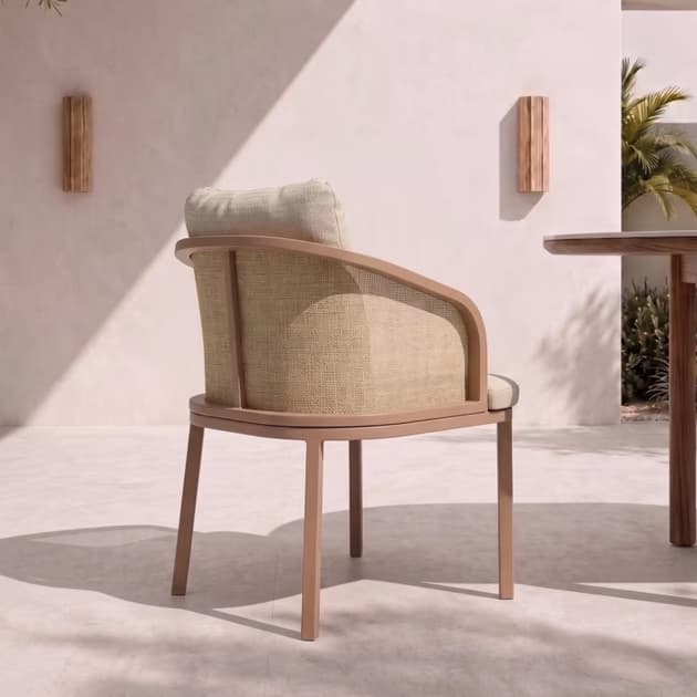 A contemporary armchair featuring a metal frame with a light brown, wood-look finish. The backrest incorporates a natural cane webbing panel, complemented by a separate upholstered back cushion and seat cushion in textured beige fabric. The chair stands on four straight, square-profile legs and has gracefully curved armrests. — 3D model