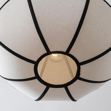 A close-up view of the underside of a fabric chandelier. The shade is constructed from light-colored, textured fabric panels, divided by dark, possibly black, binding or trim. The panels create a somewhat spherical or drum-like shape. An exposed incandescent light bulb is visible through a central opening at the bottom, with internal support structures for the shade also discernible. — 3D model