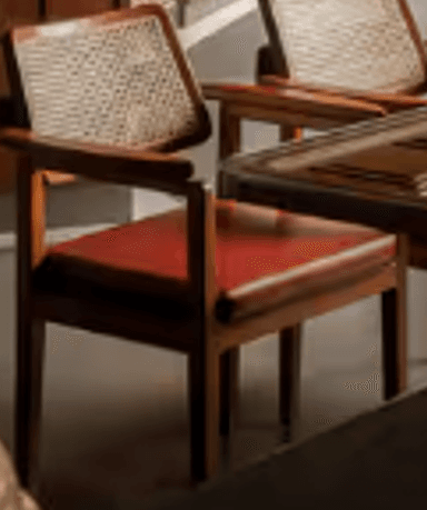 A contemporary armchair featuring a solid dark wood frame, a caned backrest, and a red upholstered seat cushion. — 3D model
