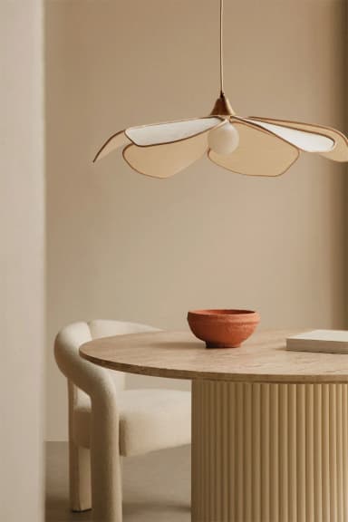 A pendant light fixture with a lampshade resembling a flower with multiple layered petals. The petals are made of a light-colored fabric or material with a darker trim. A single round bulb is visible at the center. The fixture is suspended by a thin cord and has metallic accents near the top. — 3D model