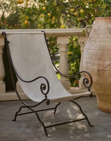 A lounge chair with an ornate wrought iron frame and a light-colored fabric sling seat and back. The metal frame features intricate scrollwork on the armrests and upper back. — 3D model