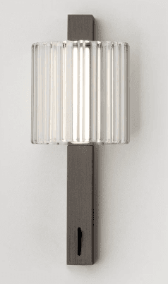 A modern wall sconce featuring a rectangular dark-finished metal backplate and a clear fluted glass cylindrical shade enclosing a vertical integrated LED light source. The design is sleek and minimalist, emphasizing clean lines and textural contrast between the metal and glass elements. — 3D model