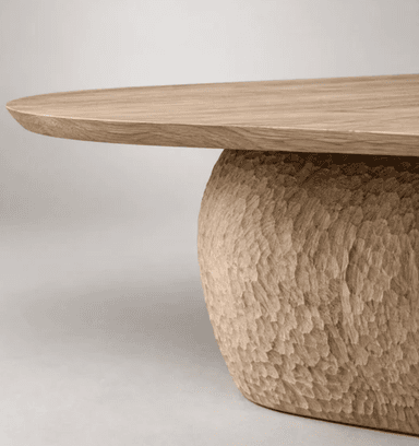 A substantial dining table featuring a light-toned, rectangular solid wood slab top with softly tapered edges, supported by a single, dark-toned, heavily sculpted and textured pedestal base with an organic, irregular form. — 3D model