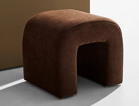 A compact, upholstered ottoman with a distinct U-shaped silhouette. The piece features a rounded top and curved sides that form an open central cavity. The upholstery appears to be a textured fabric, giving it a soft appearance. It is presented against a muted background, with strong directional lighting casting shadows. — 3D model