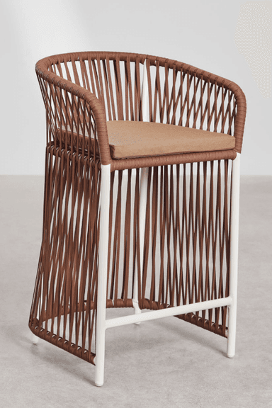 A contemporary bar stool featuring a brown woven rope seat and back, integrated armrests, and a white powder-coated metal frame. It includes a removable, light brown upholstered seat cushion. The base is an open-frame design with a horizontal footrest. — 3D model