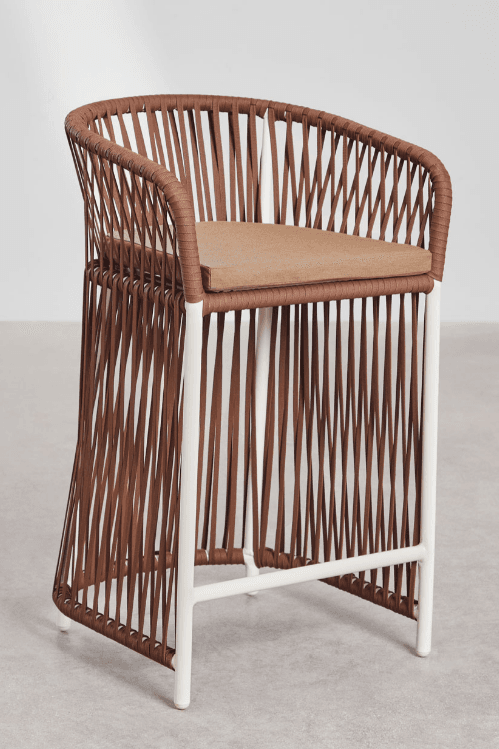 A contemporary bar stool featuring a brown woven rope seat and back, integrated armrests, and a white powder-coated metal frame. It includes a removable, light brown upholstered seat cushion. The base is an open-frame design with a horizontal footrest. — 3D model