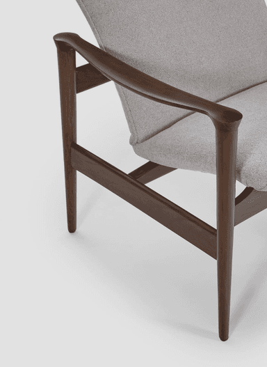 A mid-century modern armchair with a solid wood frame and upholstered seat and backrest. The frame features elegantly curved armrests and tapered legs, supporting a seat and a slightly reclined, segmented backrest. The upholstery is a textured light grey fabric. — 3D model