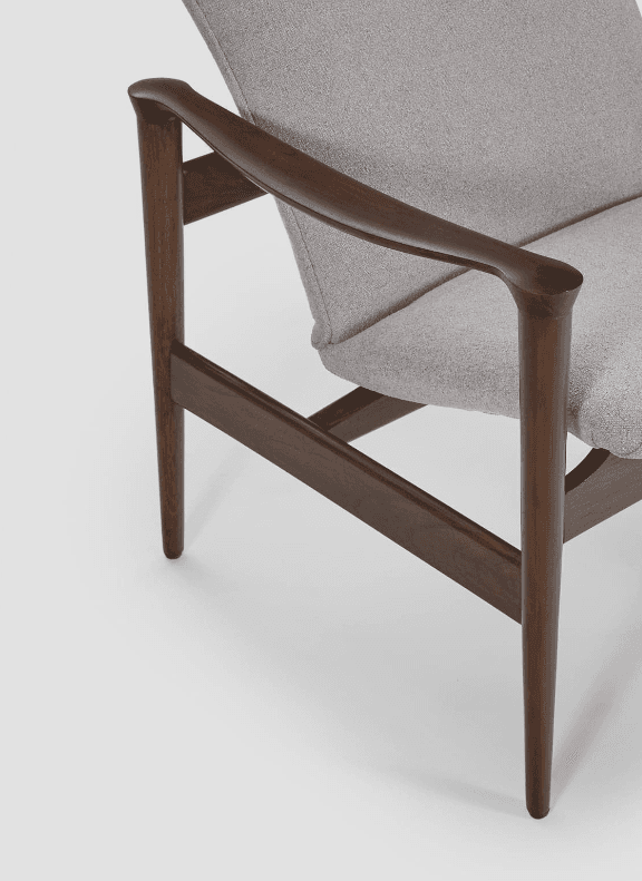 A mid-century modern armchair with a solid wood frame and upholstered seat and backrest. The frame features elegantly curved armrests and tapered legs, supporting a seat and a slightly reclined, segmented backrest. The upholstery is a textured light grey fabric. — 3D model