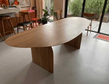 An oval coffee table with a light wood finish and two angled pedestal bases. The table has a minimalist and modern design. — 3D model