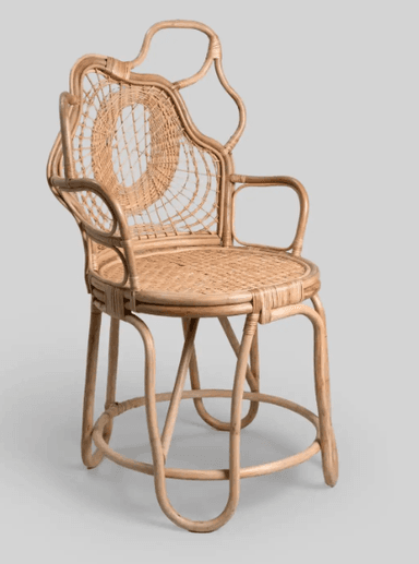 A unique armchair constructed from rattan. It features a woven seat and backrest with a distinctive circular pattern on the back. The frame is composed of bent rattan poles, creating an organic and sculptural silhouette with armrests extending from the sides and a curved top edge for the back support. The legs are also made from bent rattan poles, providing a stable base. — 3D model