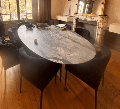 An oval-shaped coffee table featuring a grey marble-effect top with naturalistic veining, supported by four slender, tapered black metal legs. — 3D model