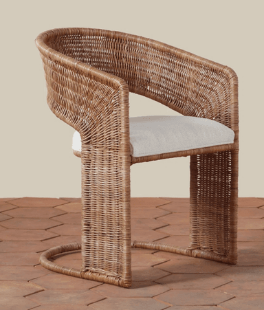 A contemporary accent chair featuring a full woven rattan construction in a natural light brown hue. The chair has a curved backrest that seamlessly transitions into integrated armrests. The frame forms a continuous loop creating a distinct sled base. A light-colored, upholstered fabric cushion provides seating. The design blends natural materials with a modern, sculptural form. — 3D model