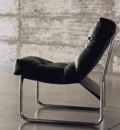 A modern lounge chair with a tufted seat and backrest, supported by a polished chrome tubular frame. The chair has a low profile and appears to be upholstered in black leather. — 3D model