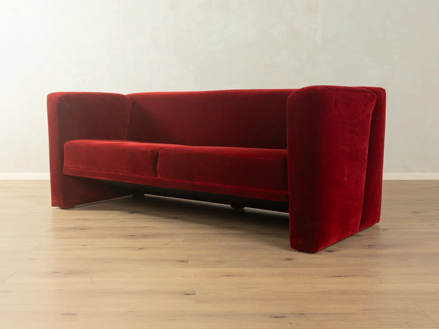 A two-seater sofa with a distinct geometric design. It features deep red velvet upholstery, high, angular armrests that extend downwards to form the base, and a single seat cushion. — 3D model
