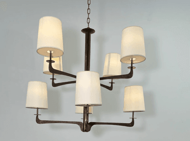 A modern multi-arm chandelier featuring a dark bronze-finished metal frame and eight tapered, drum-style fabric shades. The central column extends from a chain suspension, with eight arms branching out, each supporting an upward-facing light socket covered by a cream-colored textile shade. The metalwork exhibits a rustic or aged patina, suggesting a blend of modern design with traditional material treatment. — 3D model