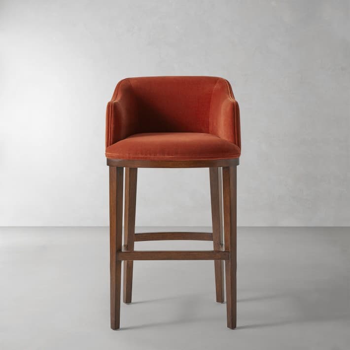 A velvet upholstered bar stool with a curved backrest and armrests, supported by a dark wooden frame. The frame consists of four straight legs connected by stretchers. — 3D model