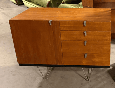 A mid-century modern style cabinet with a wood grain finish. It features a single door on the left and four drawers on the right, each with silver-toned metal pull handles. The cabinet is supported by angled metal legs, giving it a floating appearance. — 3D model