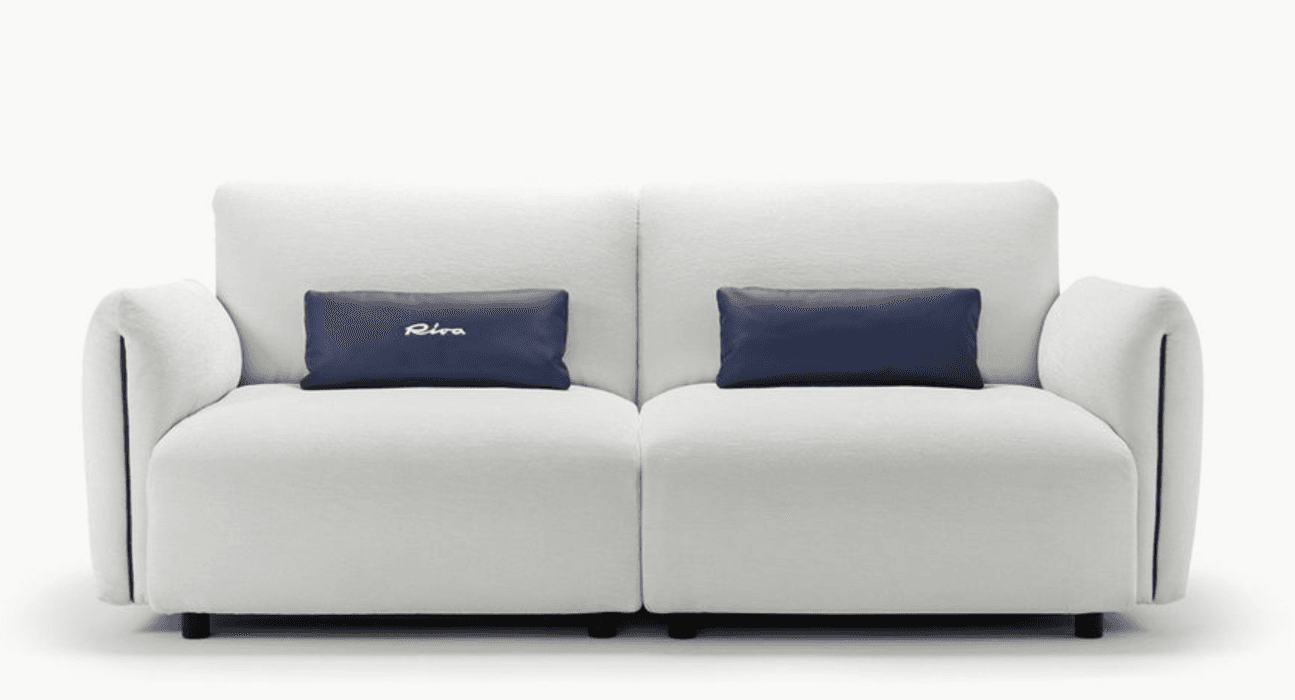 A two-seater sofa with plush white upholstery and two rectangular dark blue accent pillows. The sofa features clean lines, rounded armrests, and subtle piping detail along the edges of the armrests and seat. The pillows are placed centrally on each seat cushion. The sofa sits on low, dark legs. — 3D model