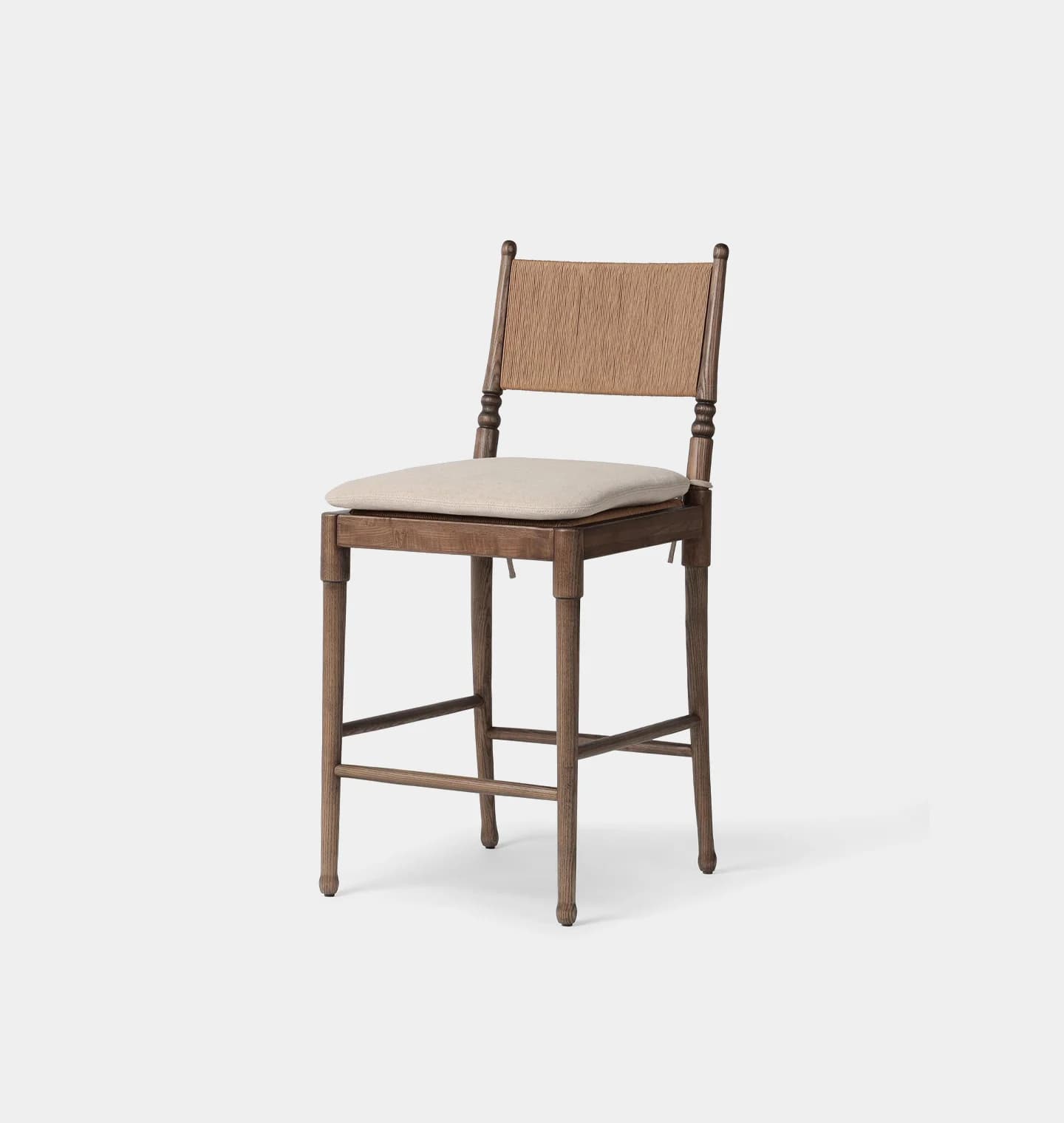 A wooden bar stool with a woven backrest and a padded seat. The stool has four legs connected by a lower support structure. The wood appears to be finished with a matte, light brown stain, and the woven backrest has a natural, earthy tone. The seat cushion is upholstered in a light beige fabric. — 3D model