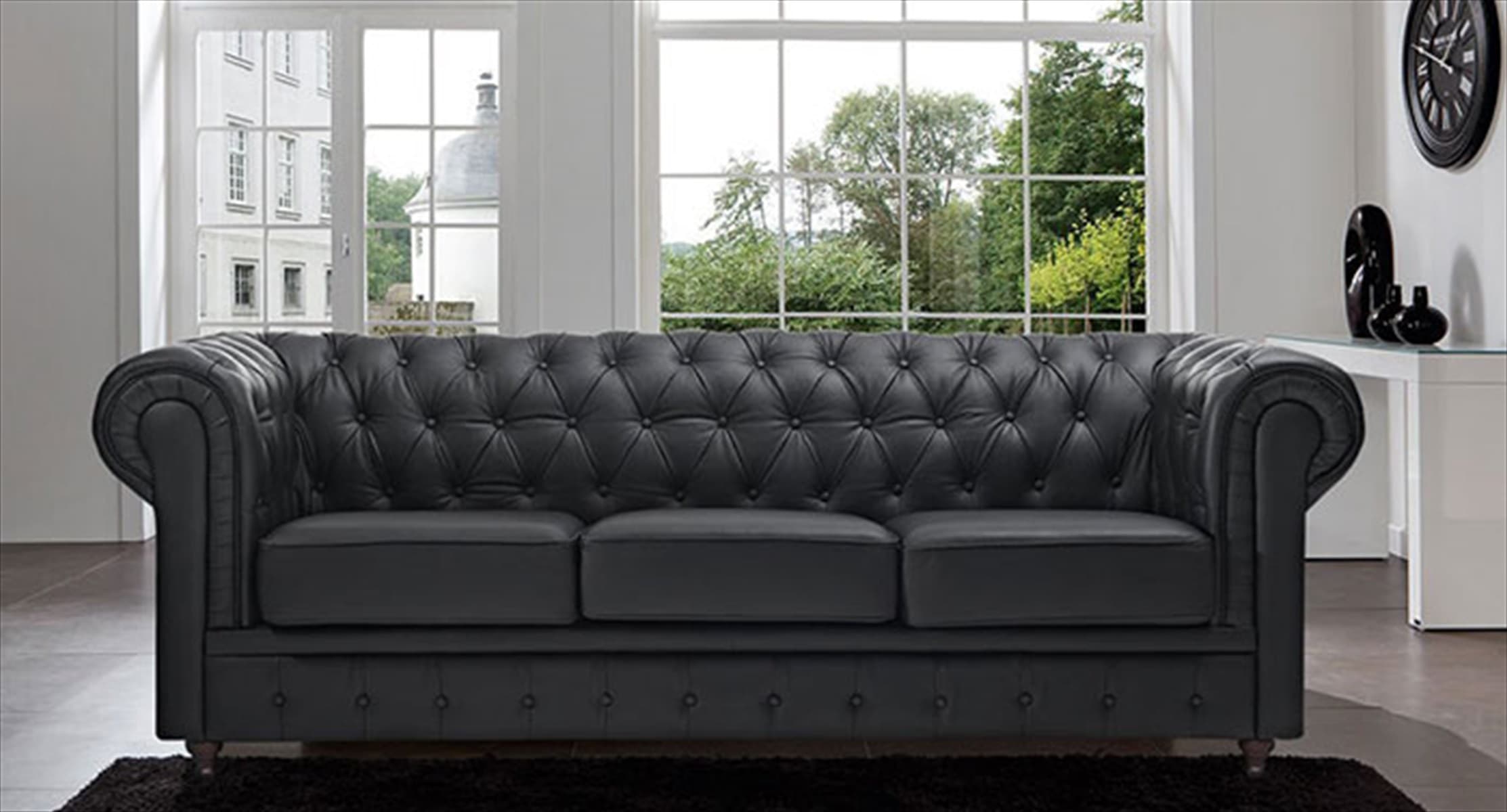 A classic three-seat Chesterfield sofa upholstered in black faux leather, featuring distinctive deep button tufting on the backrest and rolled armrests. The sofa has three individual seat cushions and rests on small, dark-finished turned legs. — 3D model