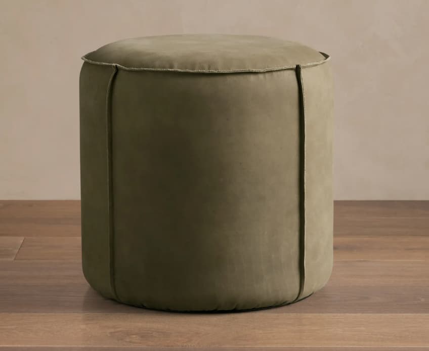 A low, cylindrical upholstered pouf in a muted olive green fabric with distinctive vertical seam details and a piped edge. — 3D model