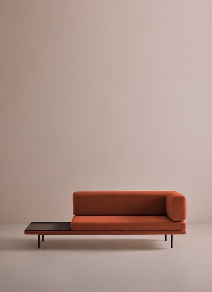 A modern chaise lounge featuring vibrant orange fabric upholstery, an integrated dark wood side table, and minimalist black metal legs. The design incorporates an L-shaped back and armrest on one side, providing ergonomic support and a defined seating area, while the opposite side extends to accommodate the side table. — 3D model