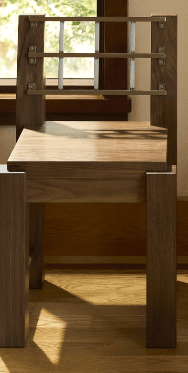 A modern wooden chair with a distinctive metal backrest. The chair features a solid wood seat and legs, with a back composed of vertical wooden uprights supporting a horizontal grid of metal bars. The construction appears sturdy and the design emphasizes geometric shapes. — 3D model
