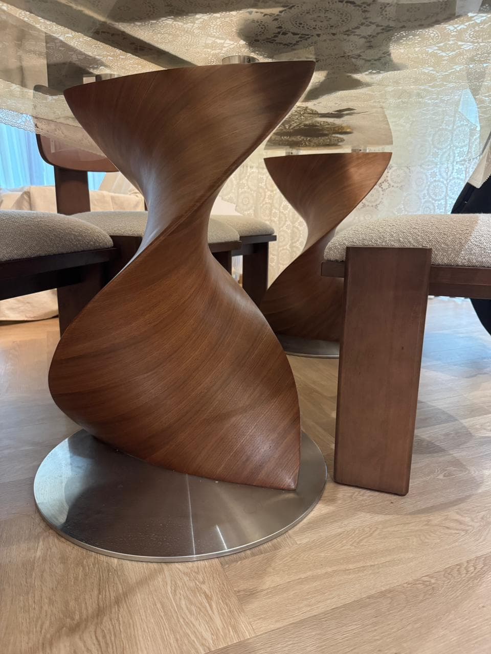 A modern sculptural accent table featuring a unique twisted, hourglass-like form crafted from rich walnut wood veneer, set upon a round, flat metal base. The design emphasizes organic curves and a dynamic silhouette, making it suitable for both functional and decorative purposes. — 3D model