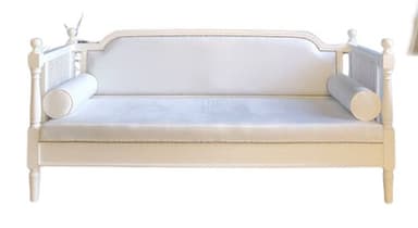 A white daybed featuring a solid wood frame, cane webbing details on the arms, and an upholstered back panel with nailhead trim. It includes a single long cushion and two cylindrical bolster pillows. — 3D model
