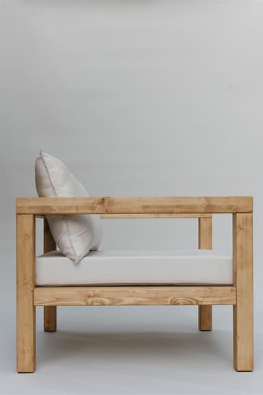 A single armchair with a solid wood frame and upholstered cushions. The frame consists of thick, square-profile wooden beams for the legs, base, and arms. The seat and back are padded with white cushions. A rectangular lumbar pillow is placed against the back cushion. — 3D model