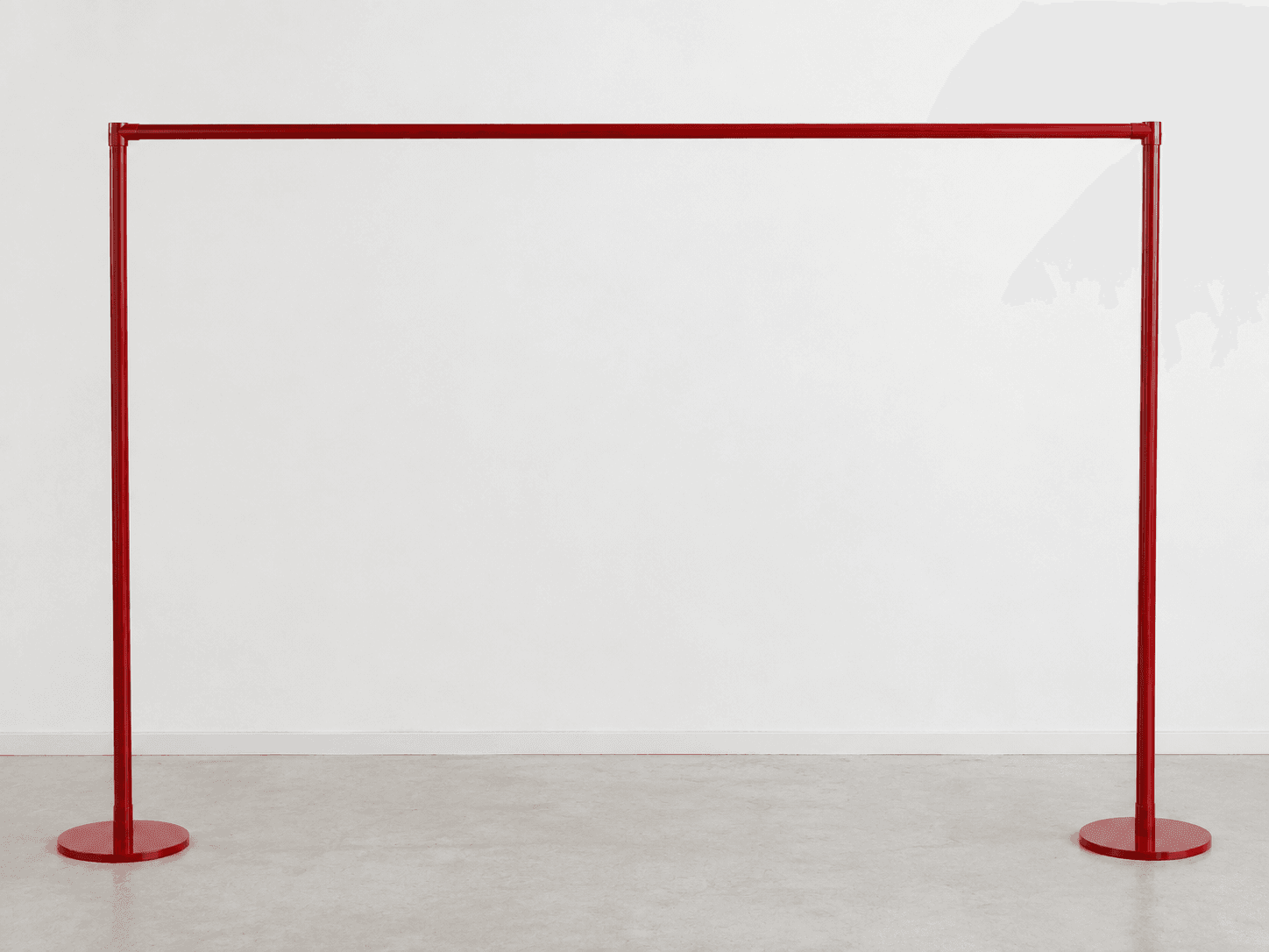 A minimalist, freestanding garment rack made from red-painted metal, featuring two vertical poles with circular bases connected by a single horizontal bar for hanging clothes. — 3D model