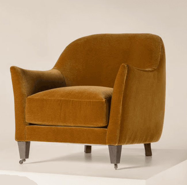 A contemporary upholstered armchair featuring a rounded back and integrated arms, deep set loose cushion, and tapered wooden legs, with the front two legs equipped with casters. The chair is covered in a golden mustard velvet fabric. — 3D model