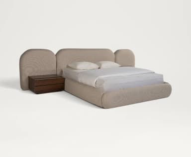 A contemporary upholstered bed featuring a low-profile frame and an extended, multi-panel headboard with rounded edges. A dark wood nightstand is positioned next to the bed, appearing to be integrated into the overall design. The bed and headboard are covered in a light beige, textured fabric. — 3D model